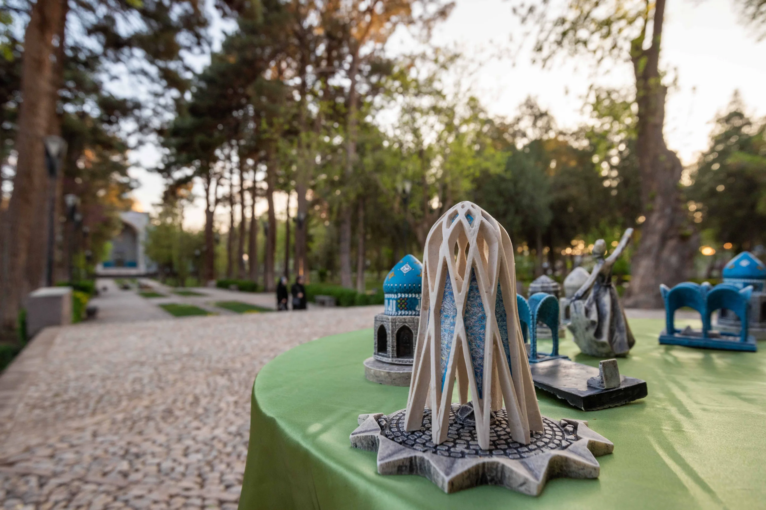 Close-up of a miniature model of the Khayyam Mausoleum on a green table, with trees and park pathways in the blurred background. Photograph by Mohammad Ataei.