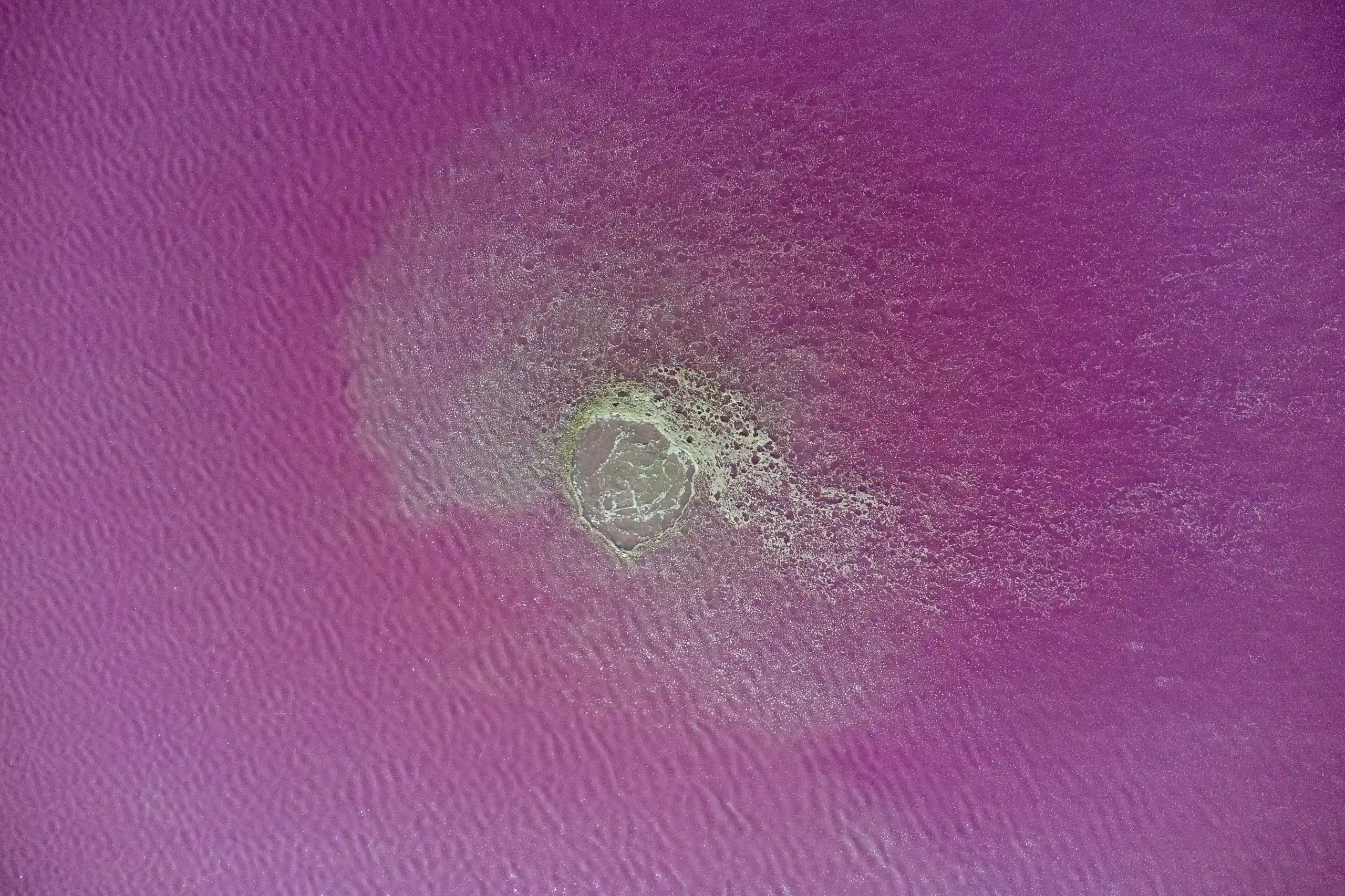 An aerial view looking straight down at the vibrant pink and purple waters surrounding the crater of Naftlijeh Mud Volcano. Photograph by Mohammad Ataei.