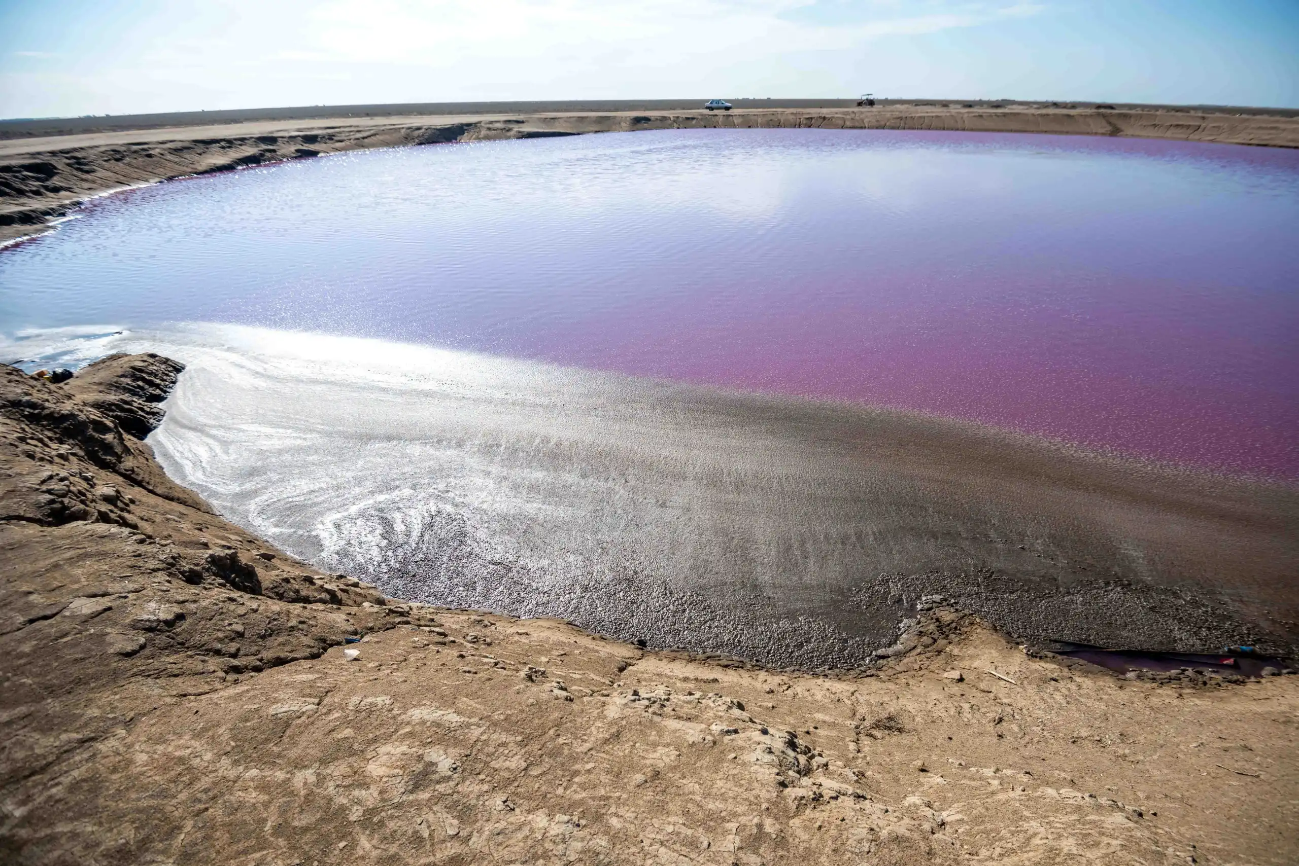 High-angle wide shot of the pink-hued pool of Naftlijeh Mud Volcano surrounded by dry earthy terrain under a bright sky in Golestan, Iran. Photograph by Mohammad Ataei.