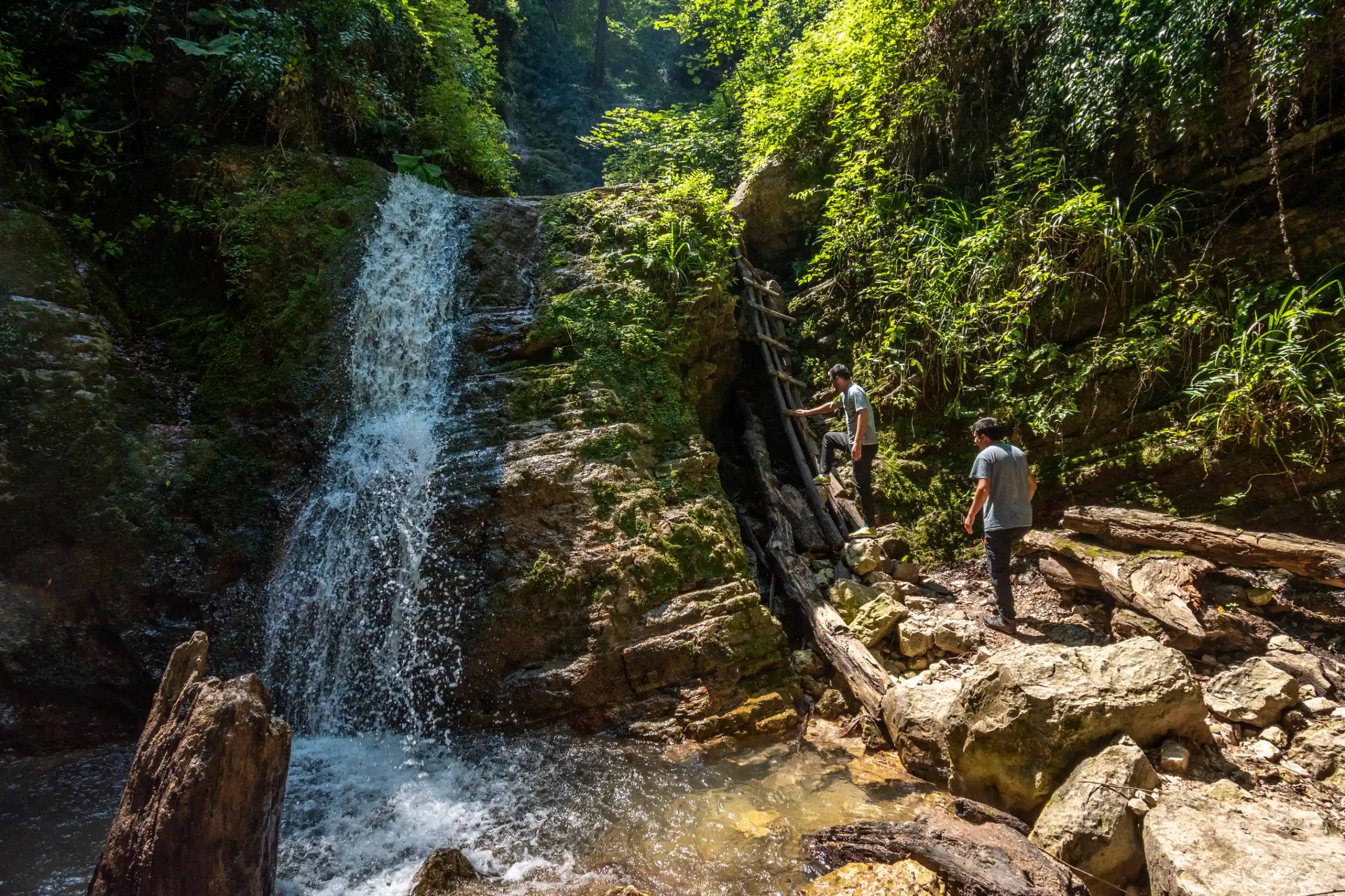 Two hikers exploring a rocky forest trail near a cascading waterfall in Gorgan, Golestan Province. Photograph by Mohammad Ataei.