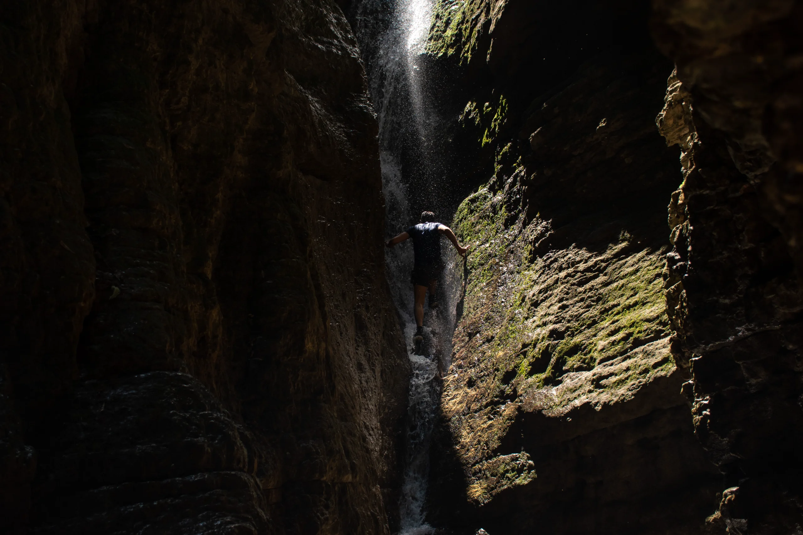 A traveler climbing a narrow rocky canyon next to a cascading waterfall at Behesht Baran in Gorgan, Iran. Photograph by Mohammad Ataei.