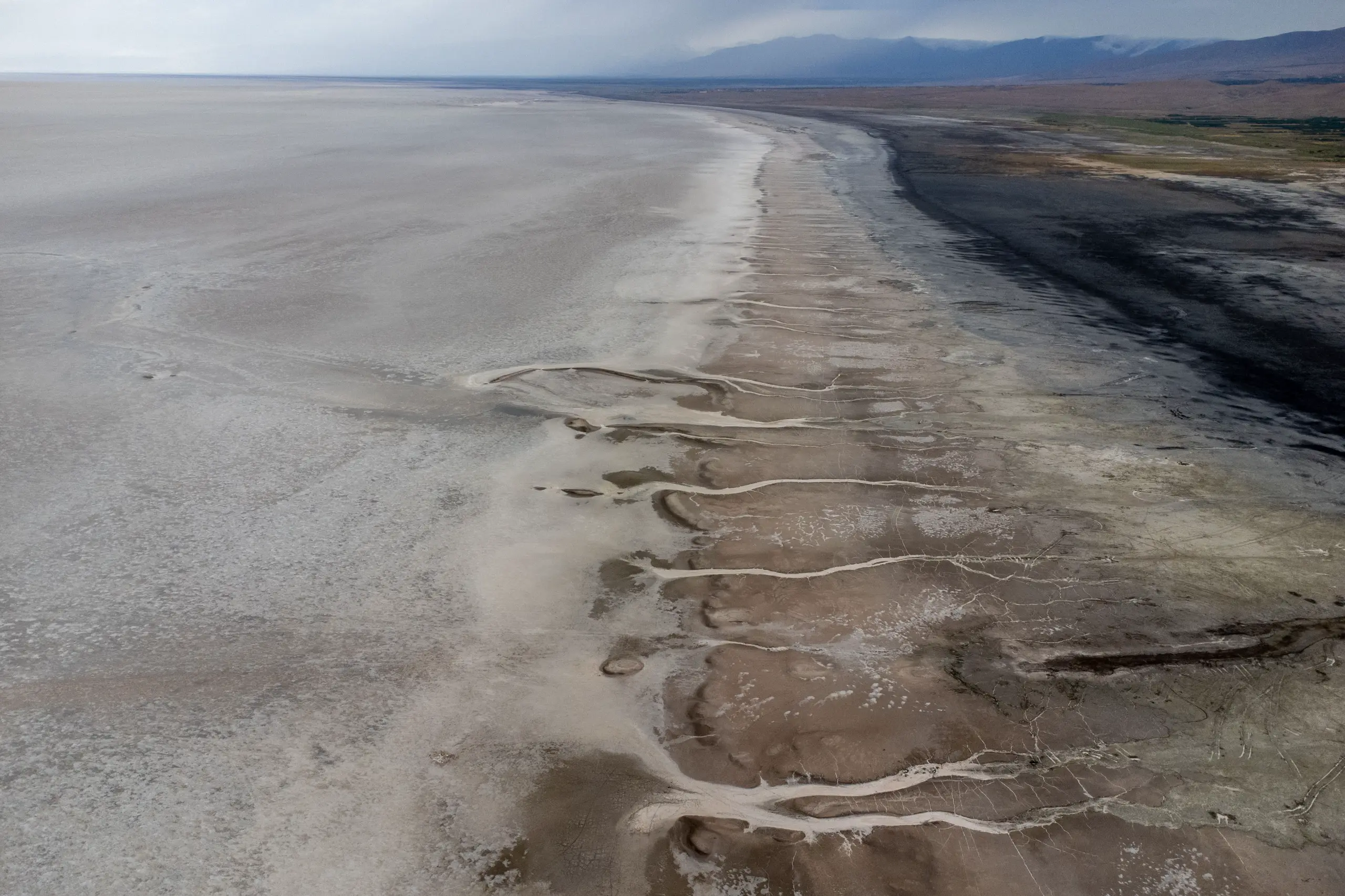 An aerial view of the vast, arid, and dried-up shoreline of Lake Urmia with patterned salt flats and distant mountains under an overcast sky. Photograph by Mohammad Ataei.