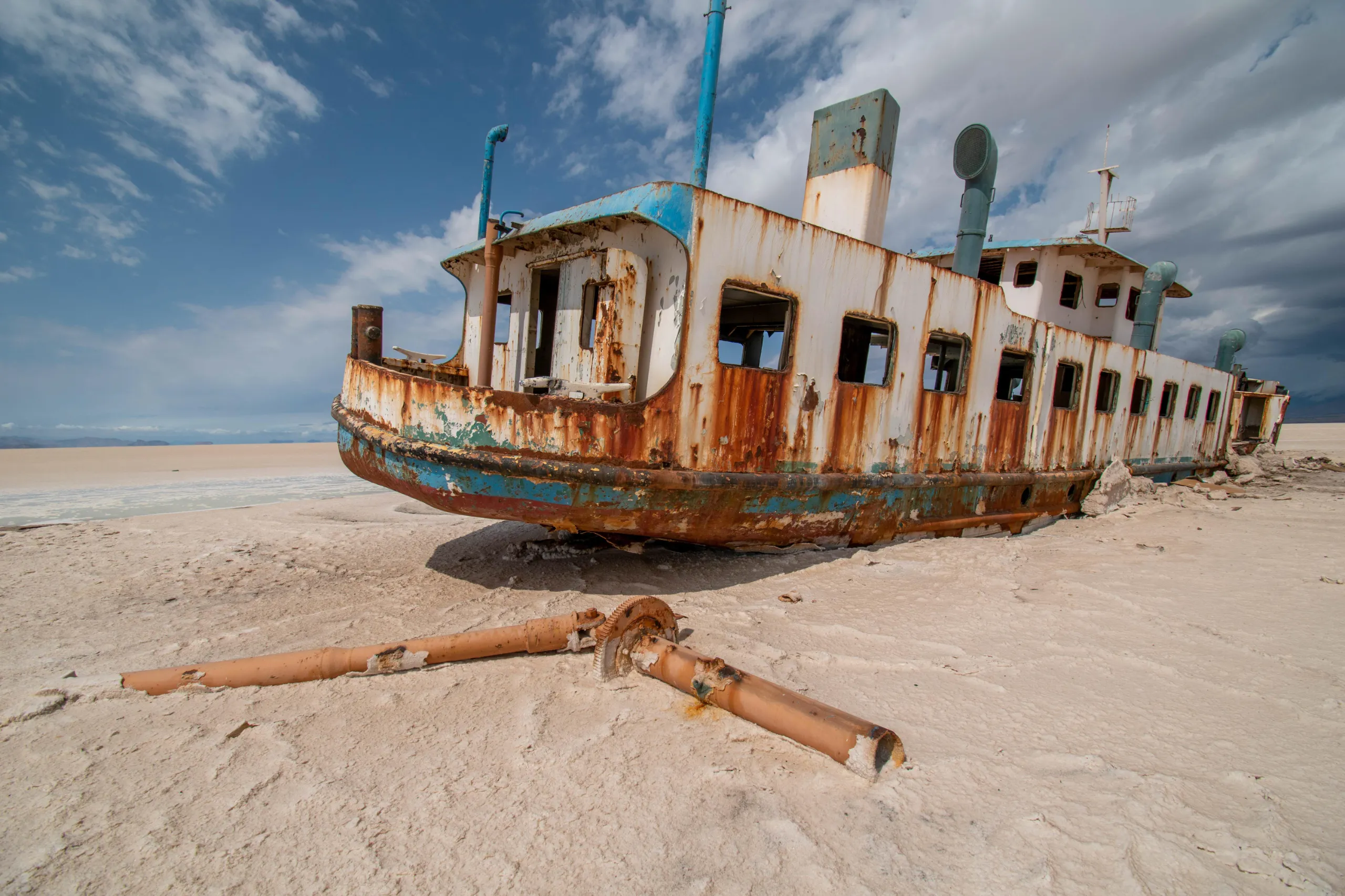 A wide-angle view of the rusted and abandoned Artemis shipwreck stranded on the dry salt flats of Lake Urmia under a partly cloudy sky. Photograph by Mohammad Ataei.