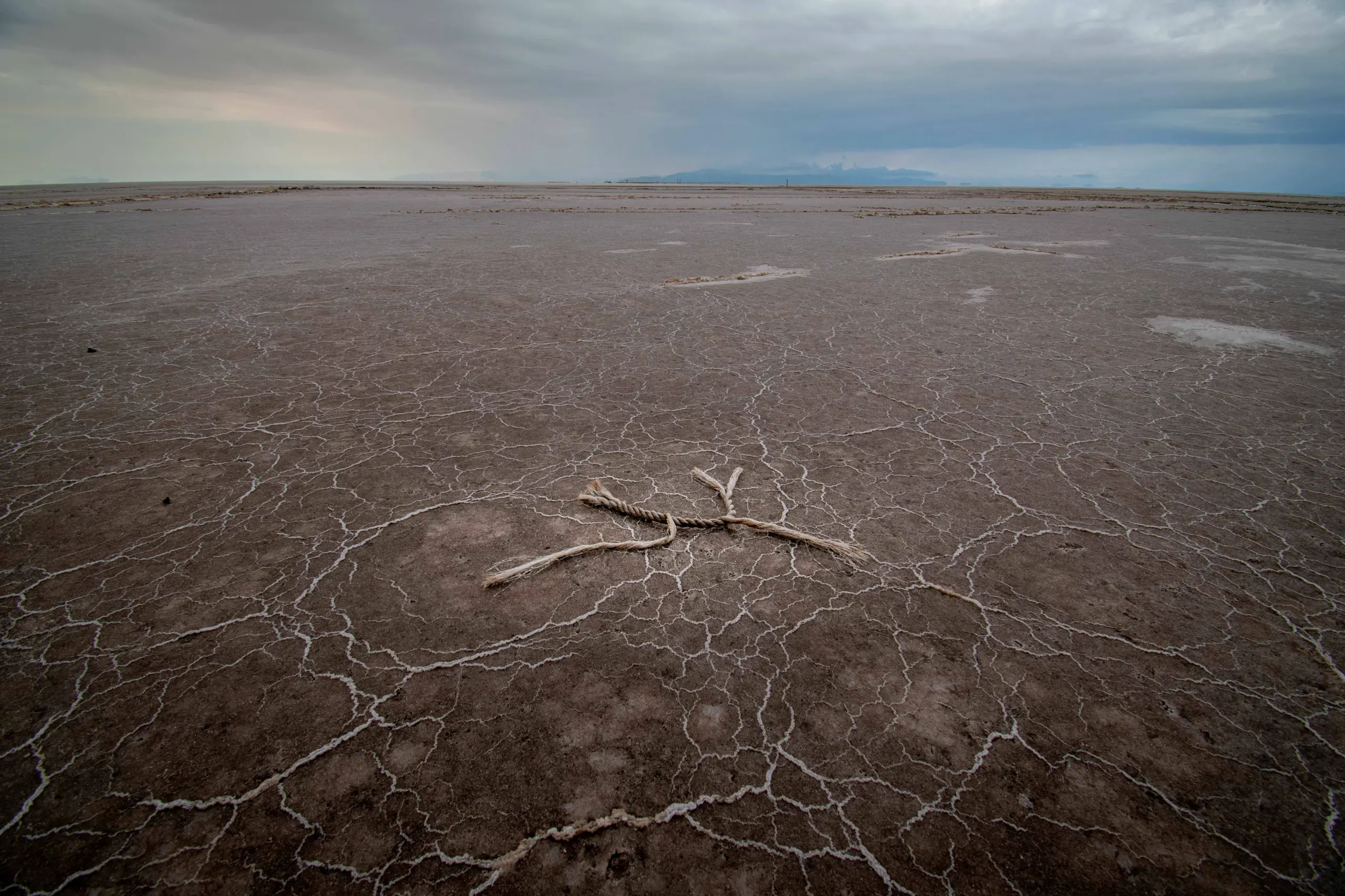 A piece of rope lies on the cracked, dry mud and salt formations of the Urmia Lake bed under a cloudy sky. Photograph by Mohammad Ataei.
