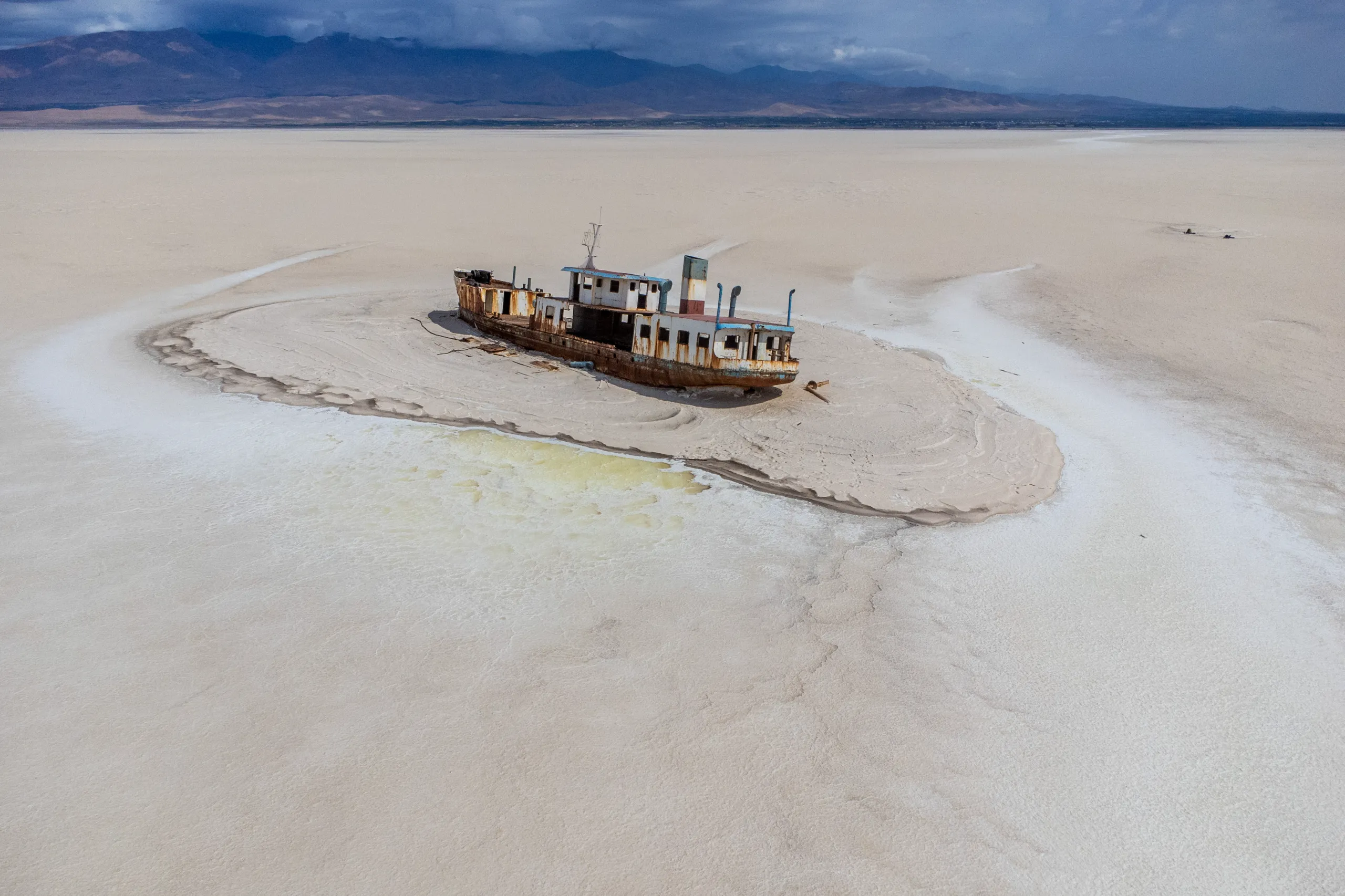 An aerial shot shows a rusted shipwreck stranded in the middle of the vast, dry white salt flats of Lake Urmia under distant mountains. Photograph by Mohammad Ataei.