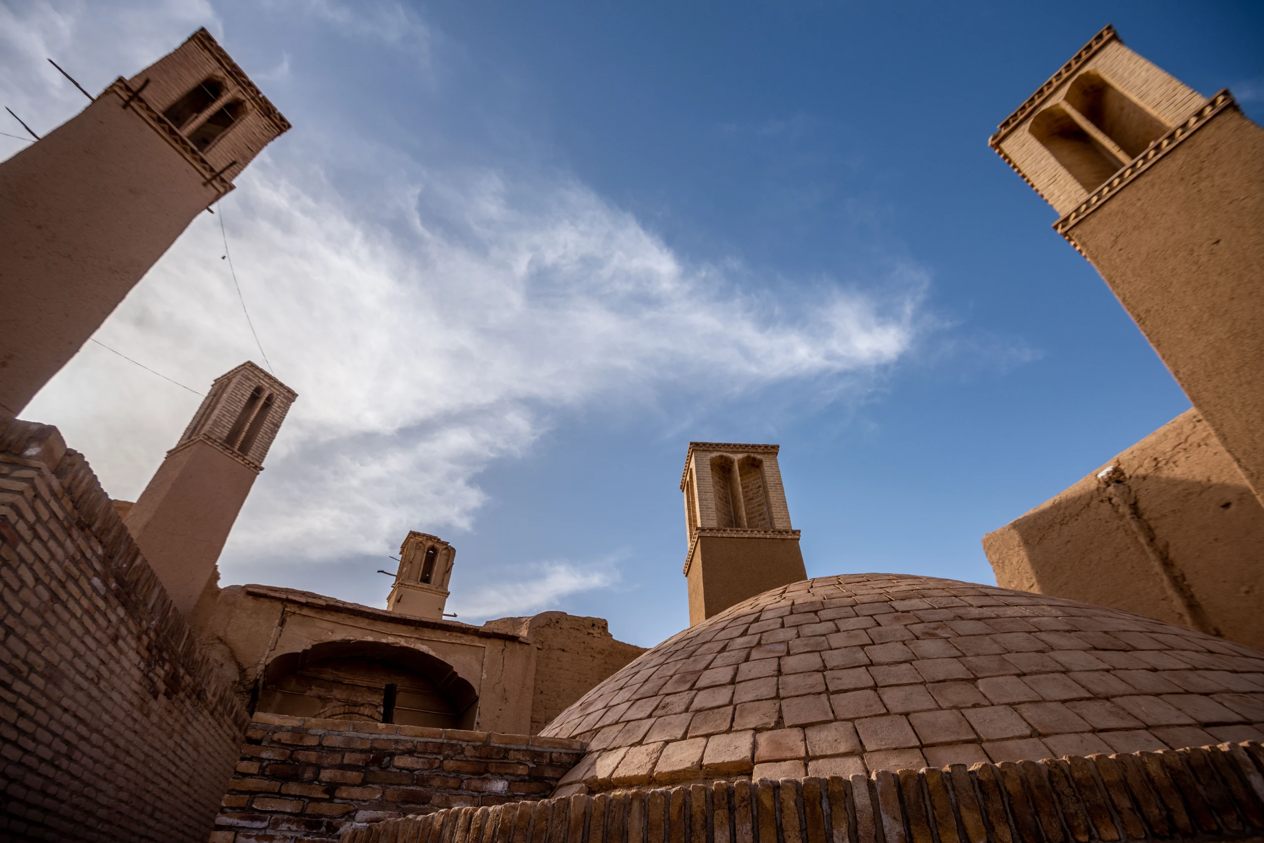 Low-angle shot of four traditional adobe windcatchers and a brick dome under a blue sky with scattered clouds in Anqa village, Yazd province. Photograph by Mohammad Ataei.